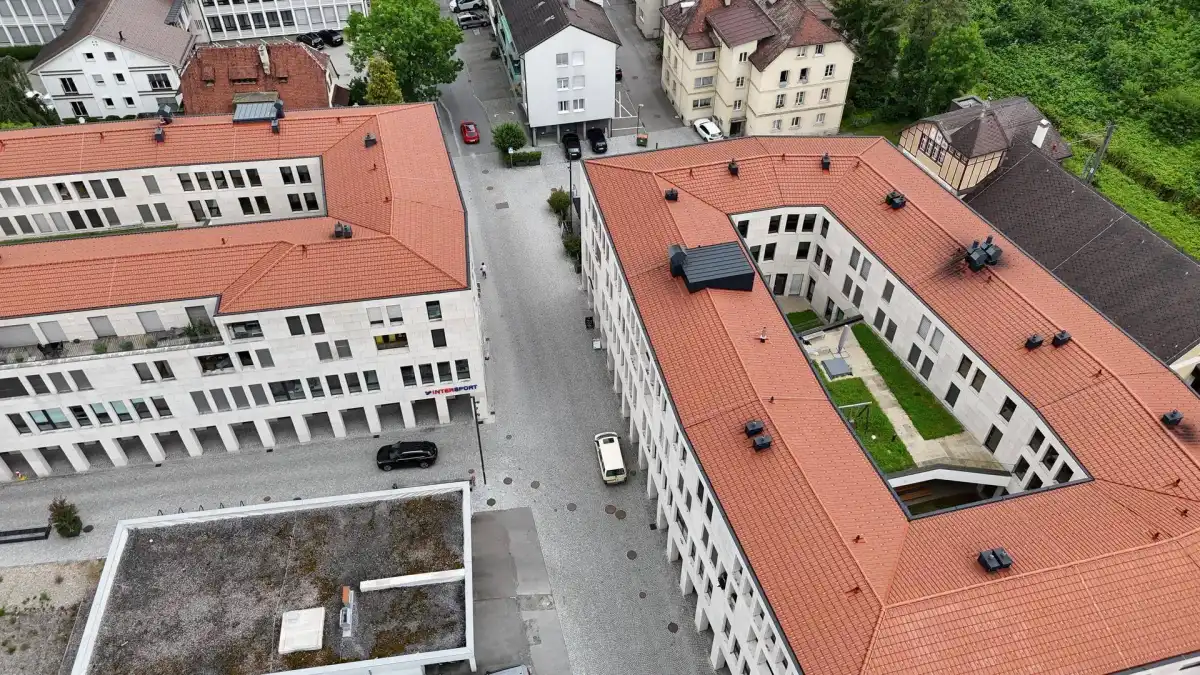Luftaufnahme eines modernen Wohnkomplexes mit roten Ziegeldächern und begrüntem Innenhof.
