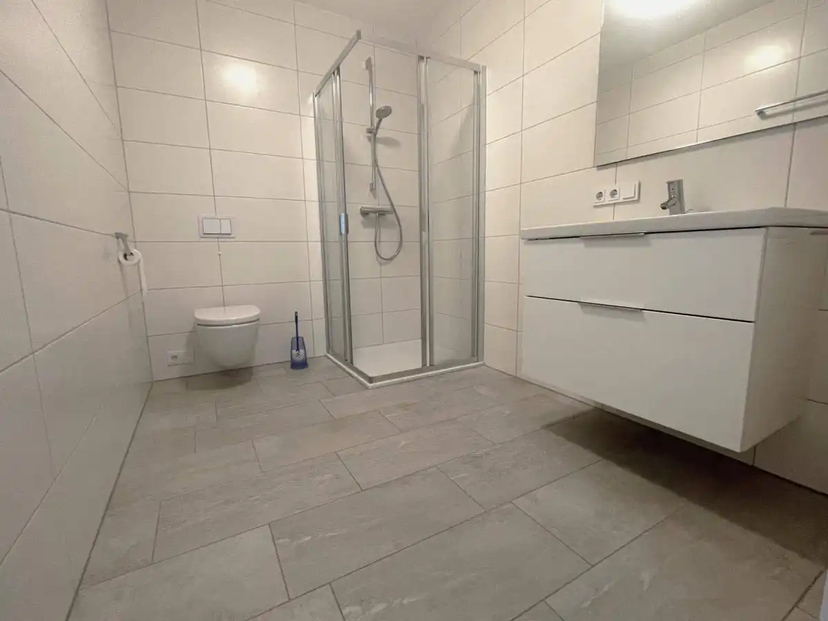 Modernes Badezimmer mit weißen Fliesen, Duschkabine und schwebendem Waschtisch.