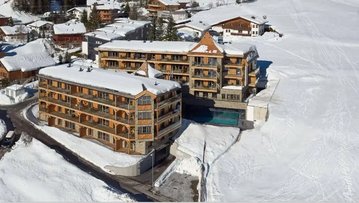Luftaufnahme der modernen Chalet-Gebäude in einer verschneiten Berglandschaft mit umliegenden Häusern.