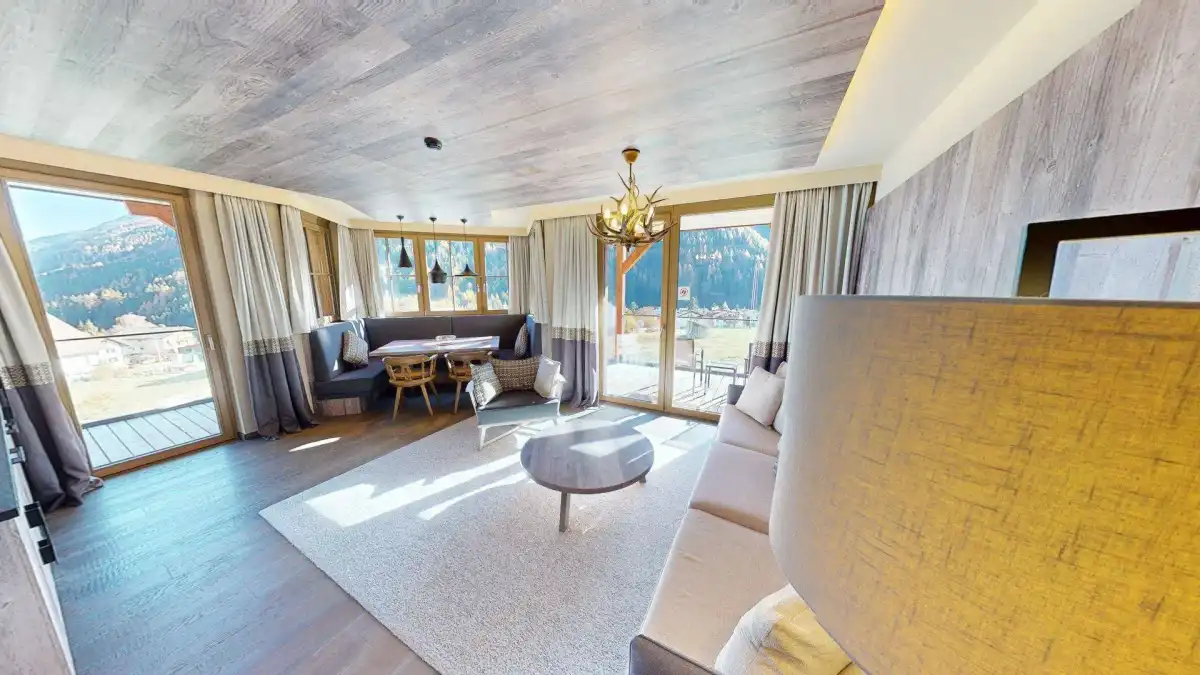 Heller Wohn- und Essbereich mit Holzboden, bequemer Couch und Zugang zum Balkon mit Bergblick.