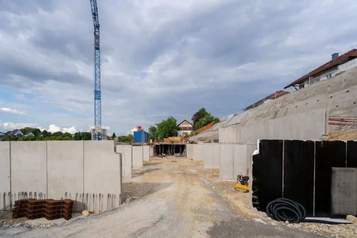 Fortgeschrittene Bauarbeiten mit freiliegenden Betonwänden und einem Baukran im Hintergrund.
