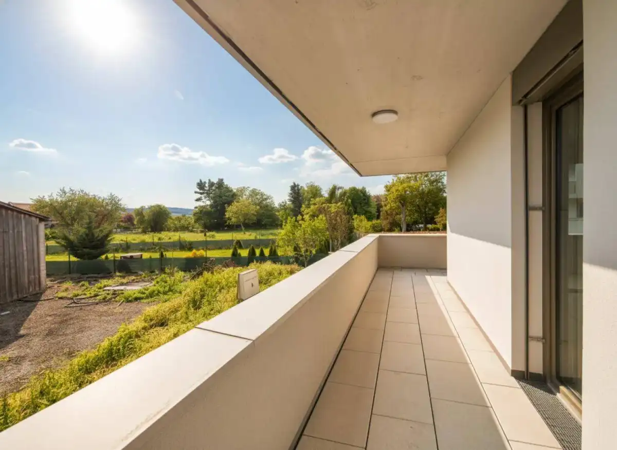 Heller Balkon mit Fliesenboden und weitem Blick ins Grüne unter strahlendem Sonnenschein.