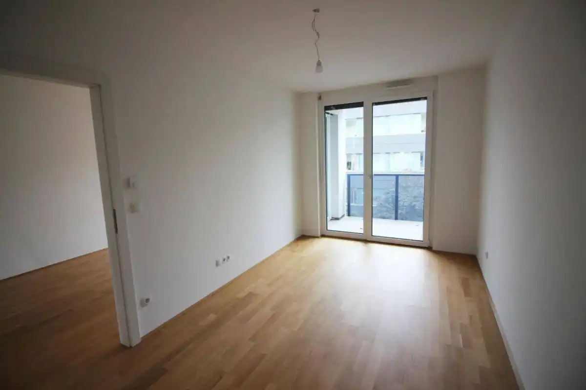 Lichtdurchflutetes Zimmer mit Holzboden und Zugang zu einem Balkon.