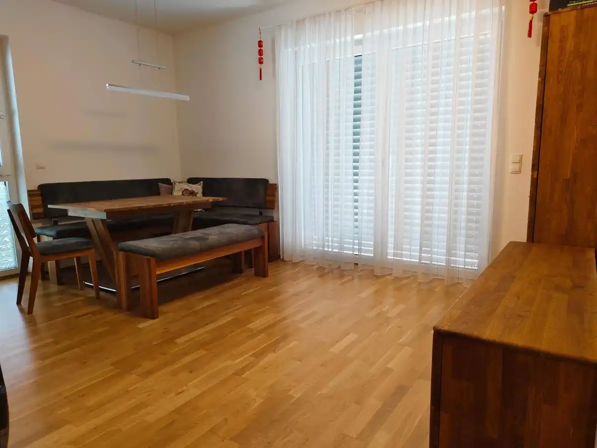 Heller Wohn- und Essbereich mit Holzboden, großem Esstisch und Zugang zum Balkon.