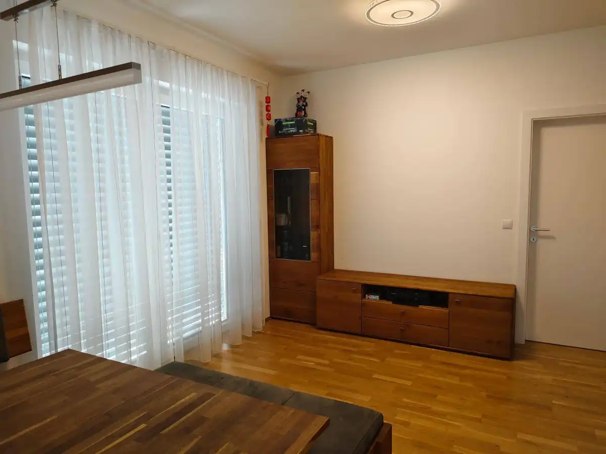 Wohnbereich mit Holzboden, modernen Möbeln und großen Fenstern mit Vorhängen.