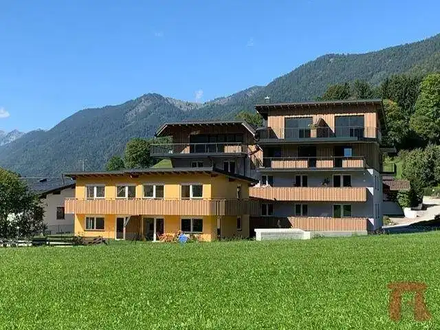 Moderner Gebäudekomplex mit Holzelementen, umgeben von grünen Wiesen und Bergen.