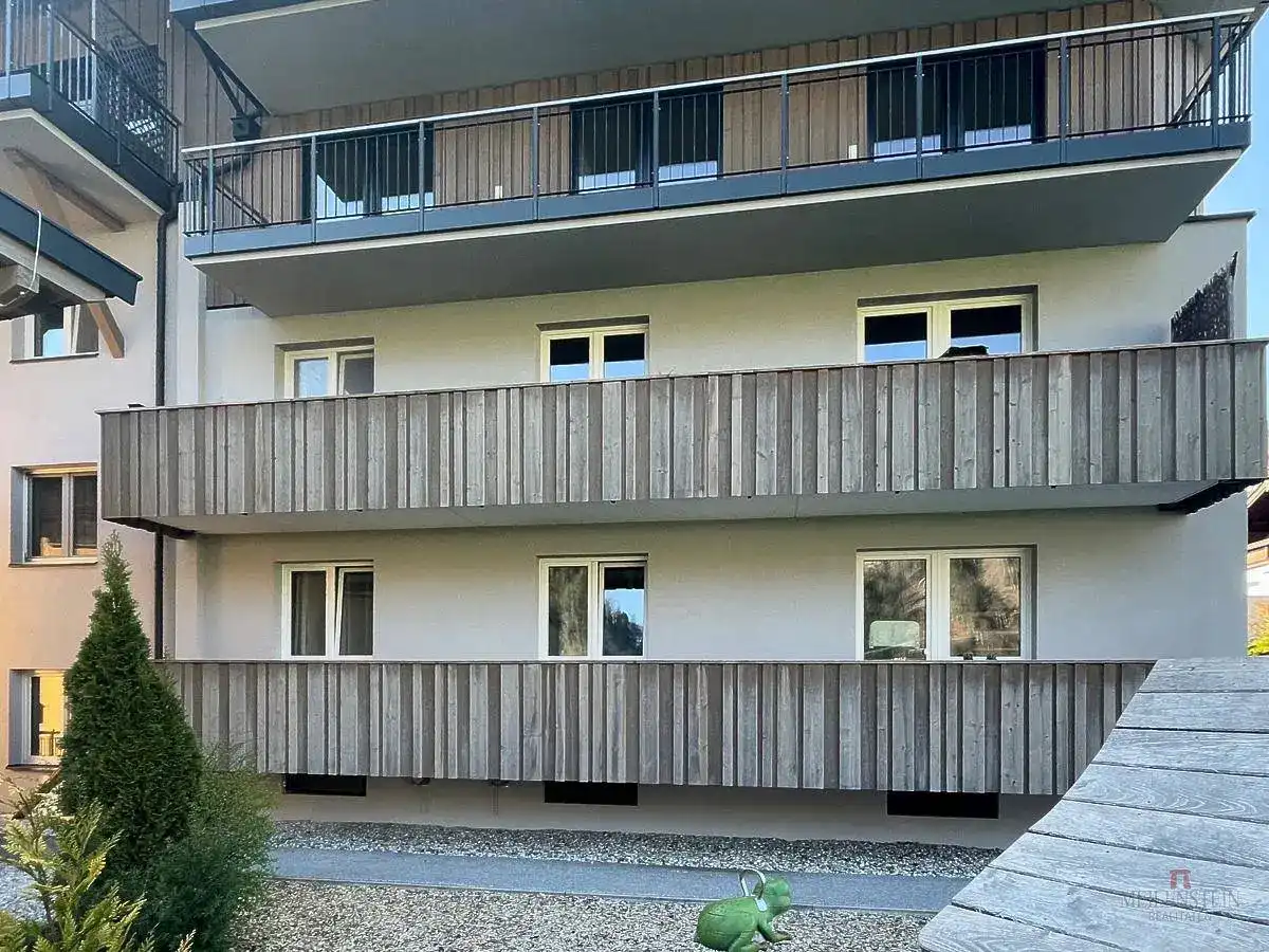 Nahaufnahme der modernen Gebäudefassade mit Holzverkleidung an den Balkonen und einem kleinen Spielgerät.