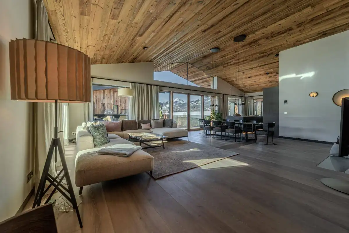 Geräumiger, lichtdurchfluteter Wohn-Essbereich mit Holzbalkendecke, modernen Möbeln und Zugang zum Balkon.