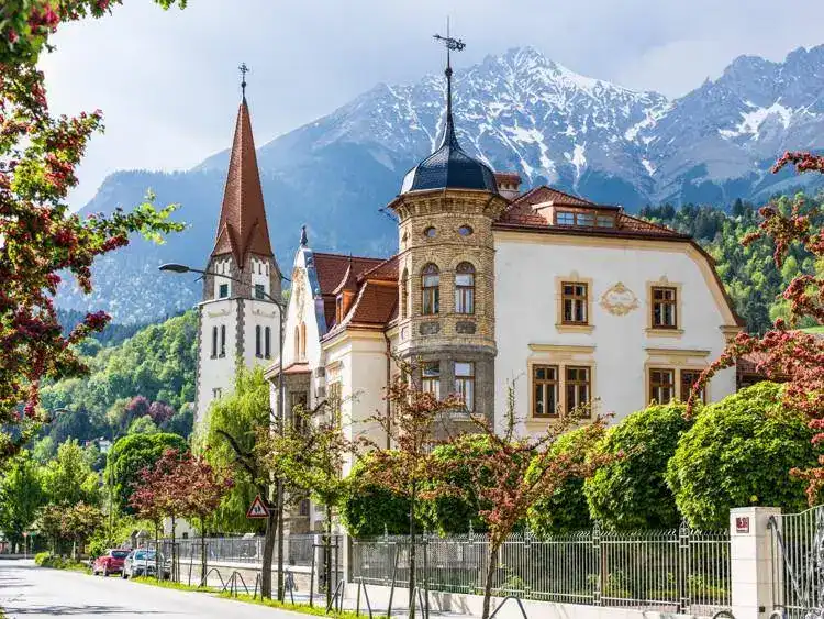 Prächtiges historisches Gebäude mit Türmen und Erker vor einer beeindruckenden Bergkulisse.