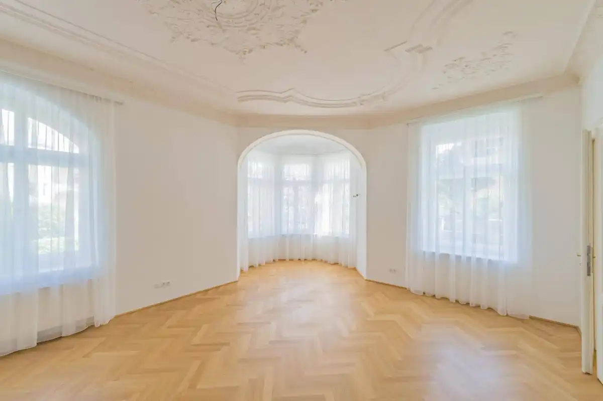 Helles Wohnzimmer mit Fischgrätparkett, Stuckdecke und großem Erkerfenster.