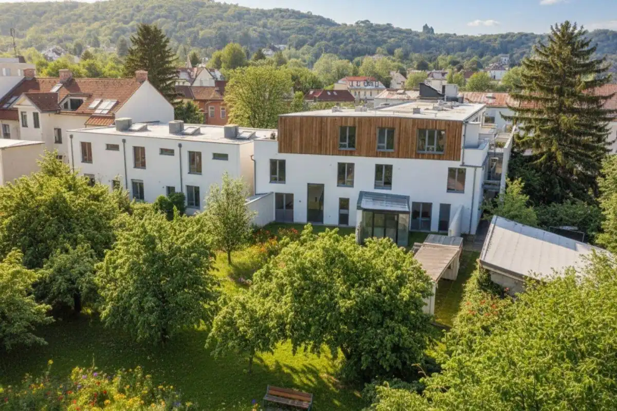 Moderne Wohnanlage mit weißer Fassade, Holzverkleidung und grüner Umgebung unter blauem Himmel.