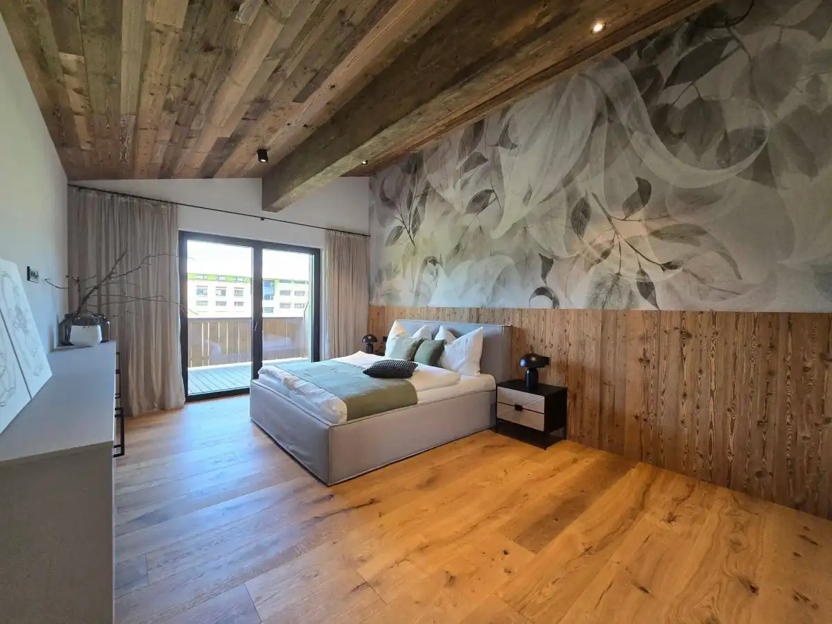 Gemütliches Schlafzimmer mit Holzboden, dekorativer Tapete und direktem Zugang zum Balkon.