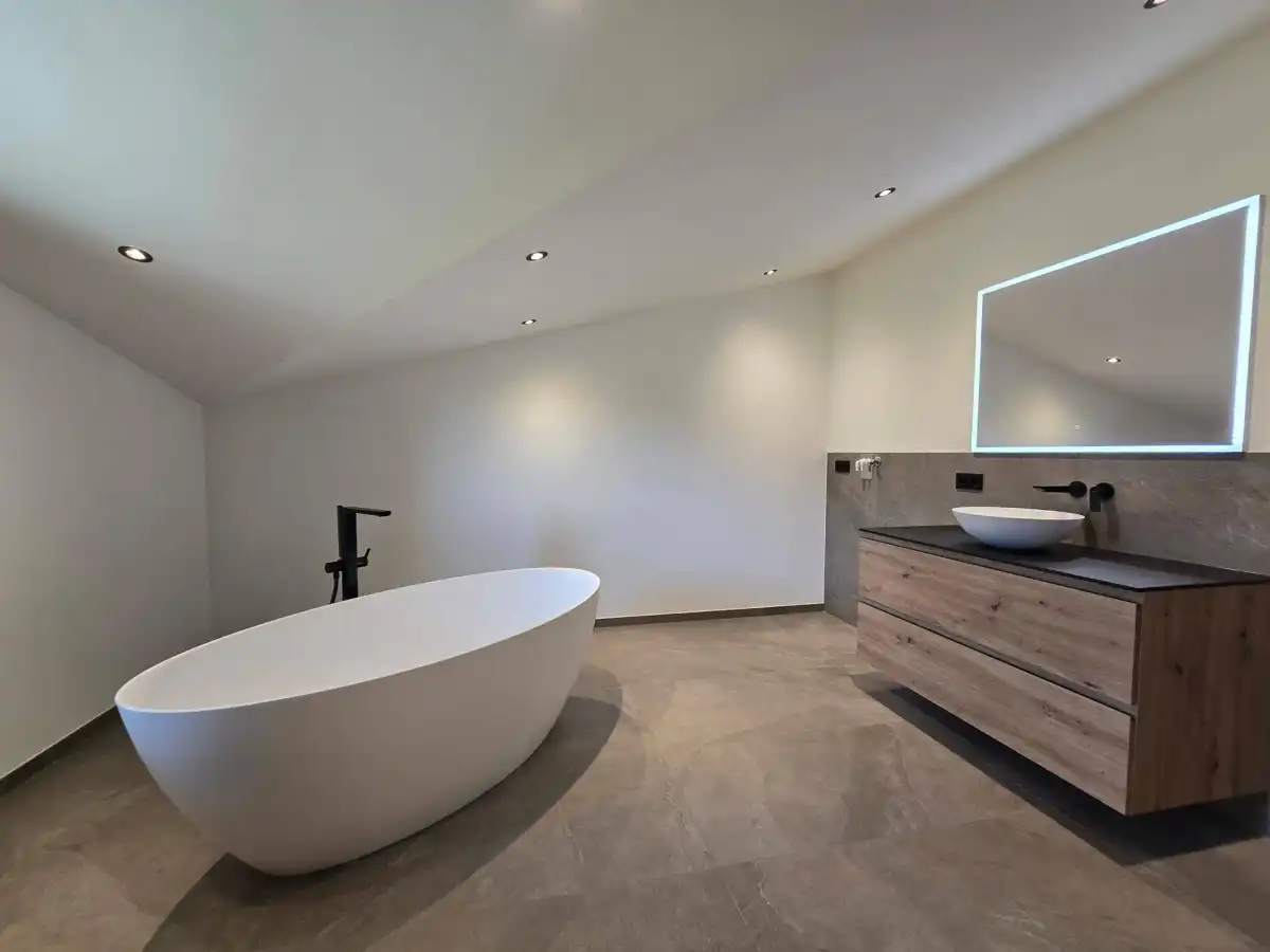 Modernes Badezimmer mit freistehender Badewanne, schwebendem Waschtisch und beleuchtetem Spiegel.