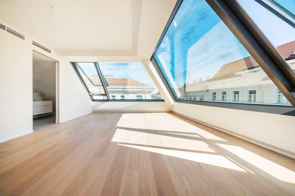 Geräumiger, heller Raum mit schrägen Fenstern und Blick auf die umliegenden Dächer, ausgestattet mit Holzparkett.