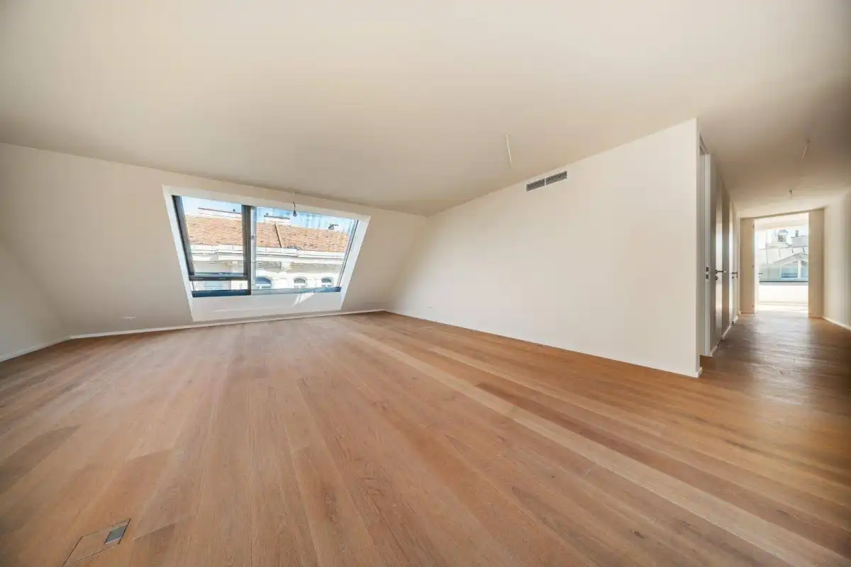 Heller Wohnraum mit schrägem Dachfenster und Zugang zu einem Flur, ausgestattet mit modernem Holzparkett.