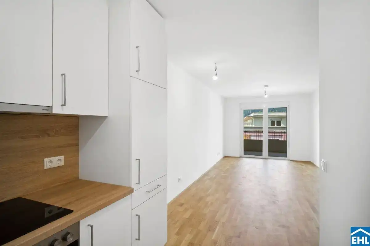 Heller Wohnbereich mit Parkettboden und Zugang zu einem Balkon, angrenzend an eine moderne Küchenzeile.