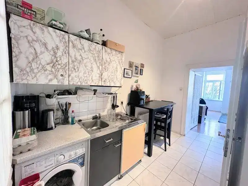 Kleine Küche mit Waschmaschine, Spüle und Esstisch, gefliestem Boden und einfacher Ausstattung.