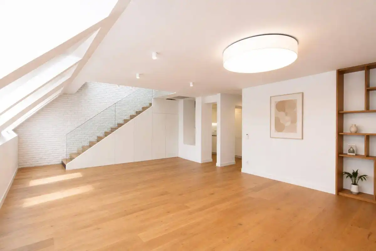 Geräumiges Wohnzimmer mit Holzboden, Dachschrägen und einer modernen Treppe mit Glasgeländer.