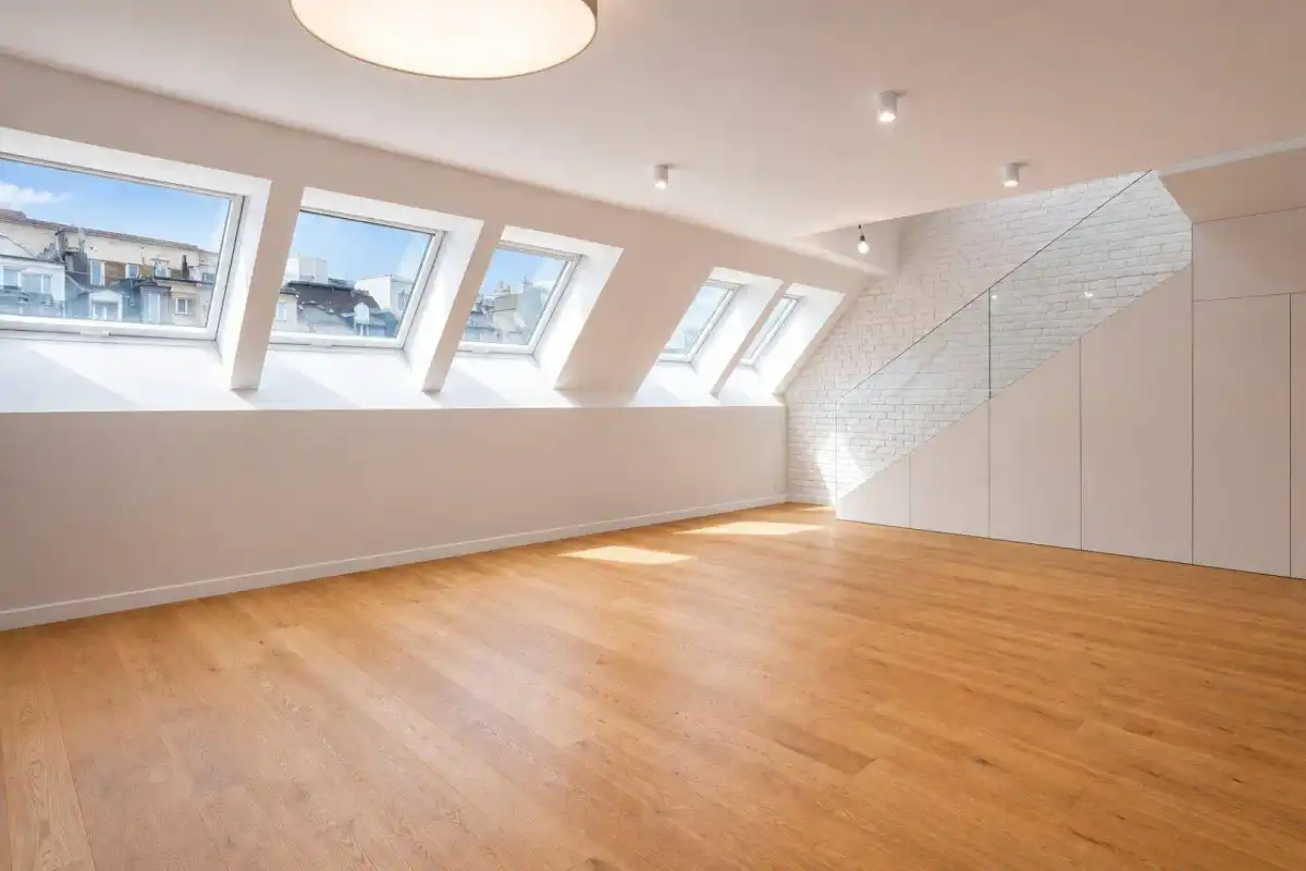 Lichtdurchflutetes Wohnzimmer mit Holzboden, Dachschrägen und mehreren Dachfenstern mit Stadtblick.