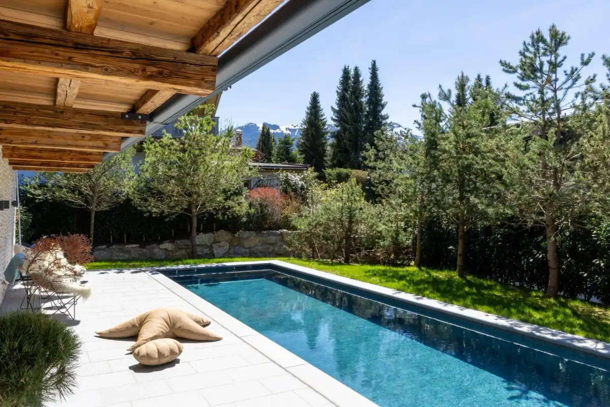 Terrasse mit Pool und Bergblick, umgeben von grüner Natur und Bäumen.