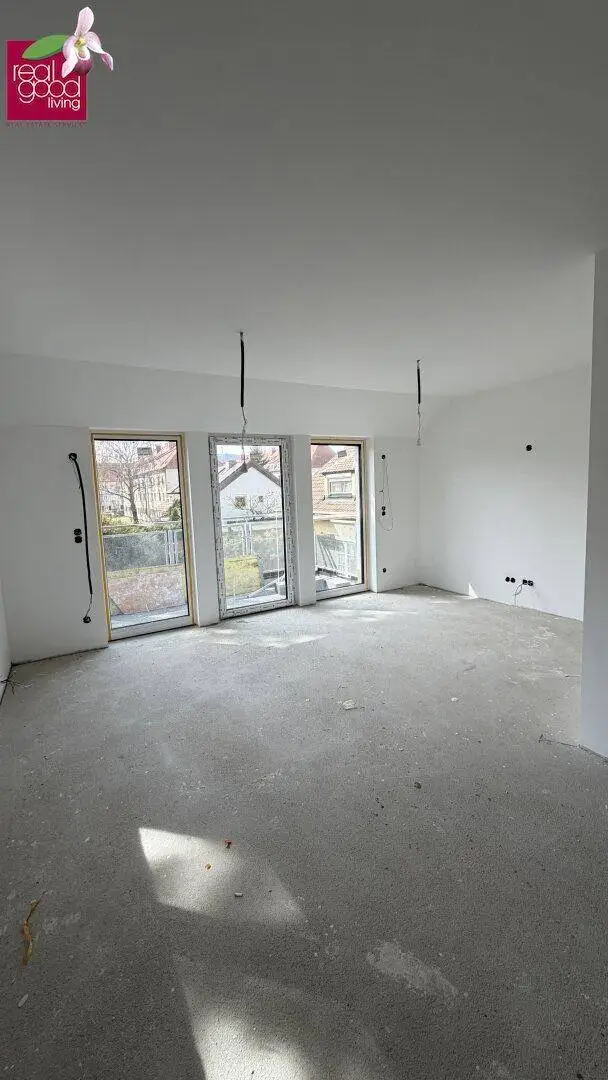 Heller Innenraum im Rohbau mit großen Fenstern und Betonboden, bereit für den Ausbau.