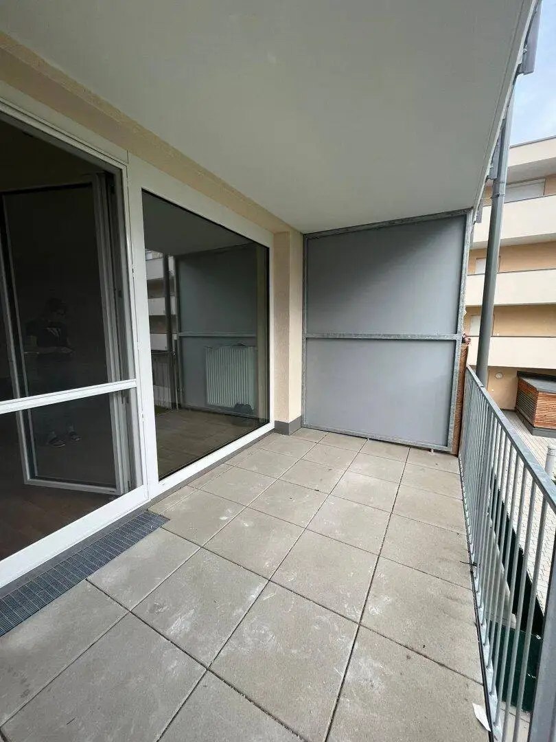 Geräumiger Balkon mit Fliesenboden und großen Fenstern, der viel Tageslicht in die Wohnung lässt.