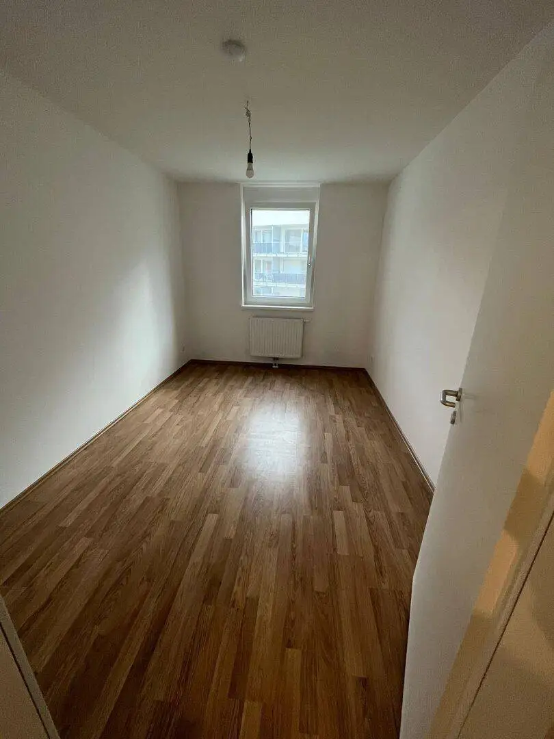 Helles Schlafzimmer mit Laminatboden und Fenster, das viel Tageslicht hereinlässt.