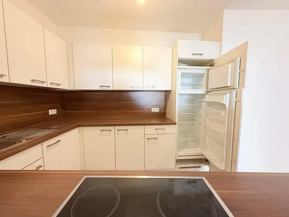 Funktionale Küche mit weißen Schränken, Holzoptik-Arbeitsplatten und integriertem Kühlschrank.