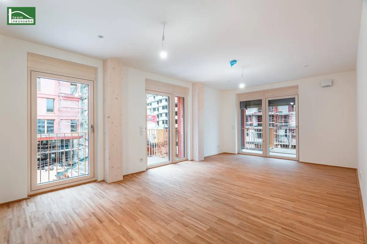 Geräumiges Wohnzimmer mit hellem Holzboden und mehreren französischen Balkonen.