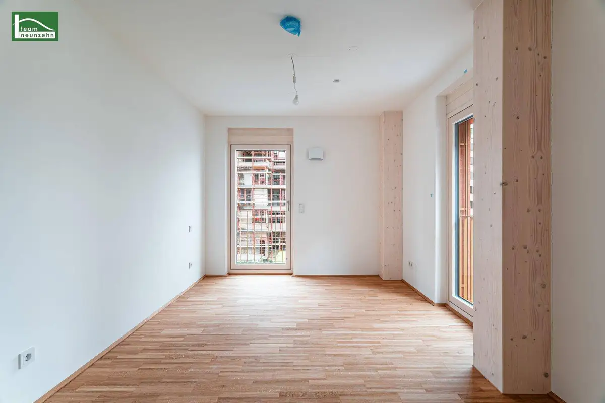 Leerer Raum mit Holzboden und zwei Fenstern, eines davon mit französischem Balkon.