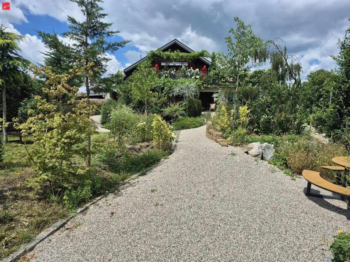 Einfamilienhaus mit weitläufigem Garten, Kiesweg und vielfältiger Bepflanzung an einem sonnigen Tag.