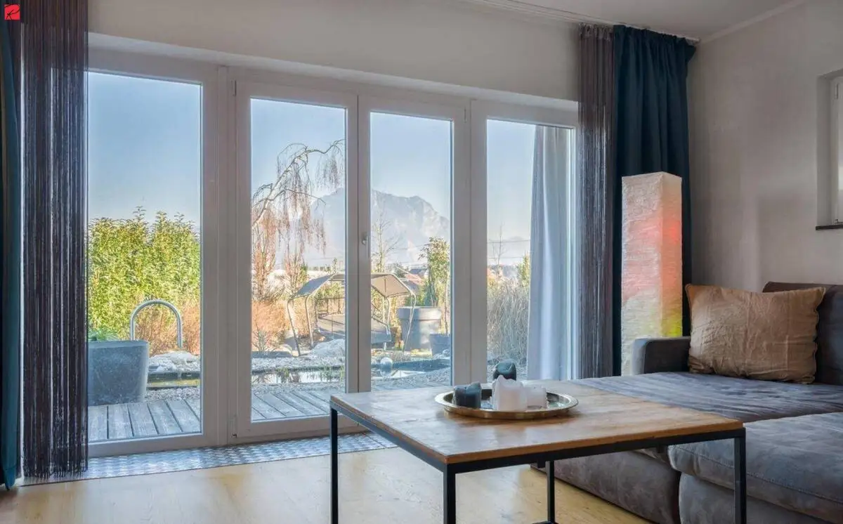 Helles Wohnzimmer mit großen Fenstern, die einen Blick auf die Terrasse und die Berge bieten.