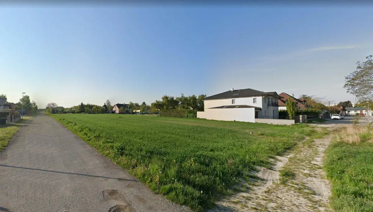 Offenes Feld mit einem Feldweg im Vordergrund und Wohngebäuden am Horizont.