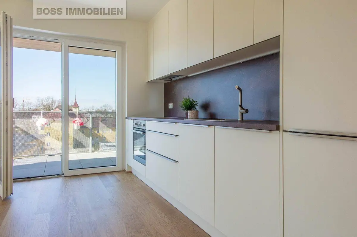 Helle Küche mit modernen Einbauschränken, Holzboden und Zugang zum sonnigen Balkon.