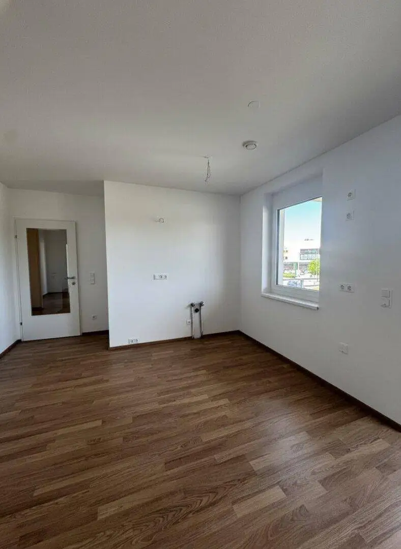 Heller Raum mit Laminatboden, weißen Wänden und Anschlussmöglichkeiten für eine Küche.