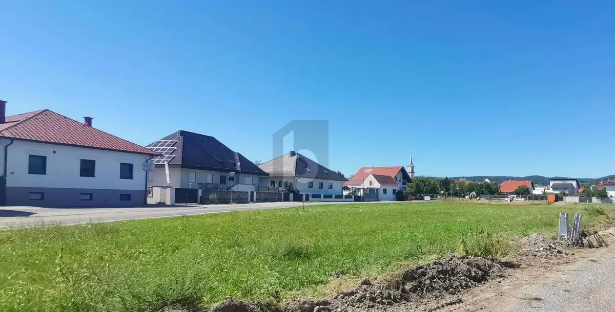 Weitläufiger Blick über eine grüne Wiese auf eine Reihe von Wohnhäusern, darunter eines mit Solaranlage.
