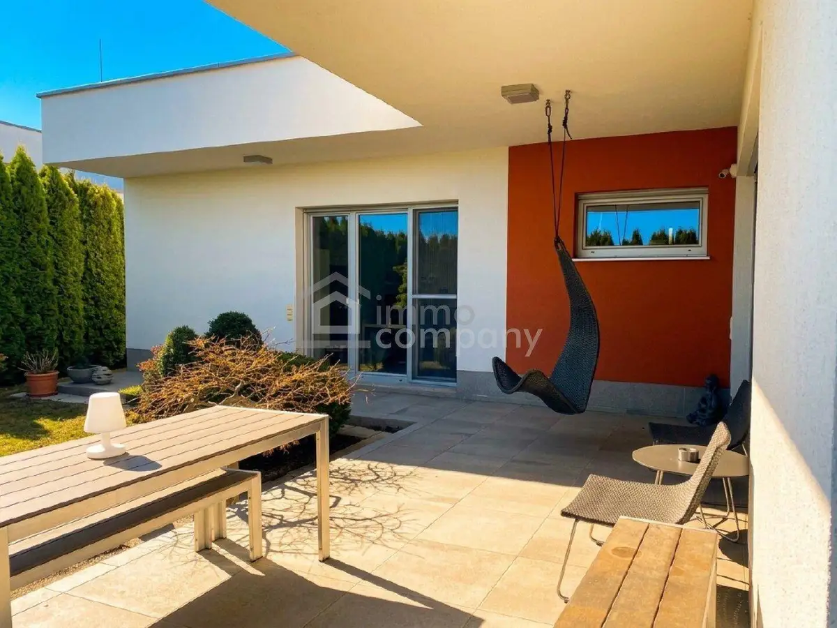 Überdachte Terrasse mit modernen Gartenmöbeln, Hängesessel und Zugang zum Gartenbereich.