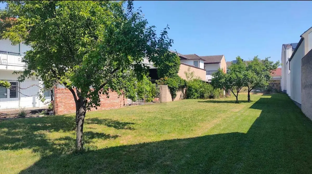Weitläufiger Garten mit Rasen und Bäumen, umgeben von Wohngebäuden und Mauern.