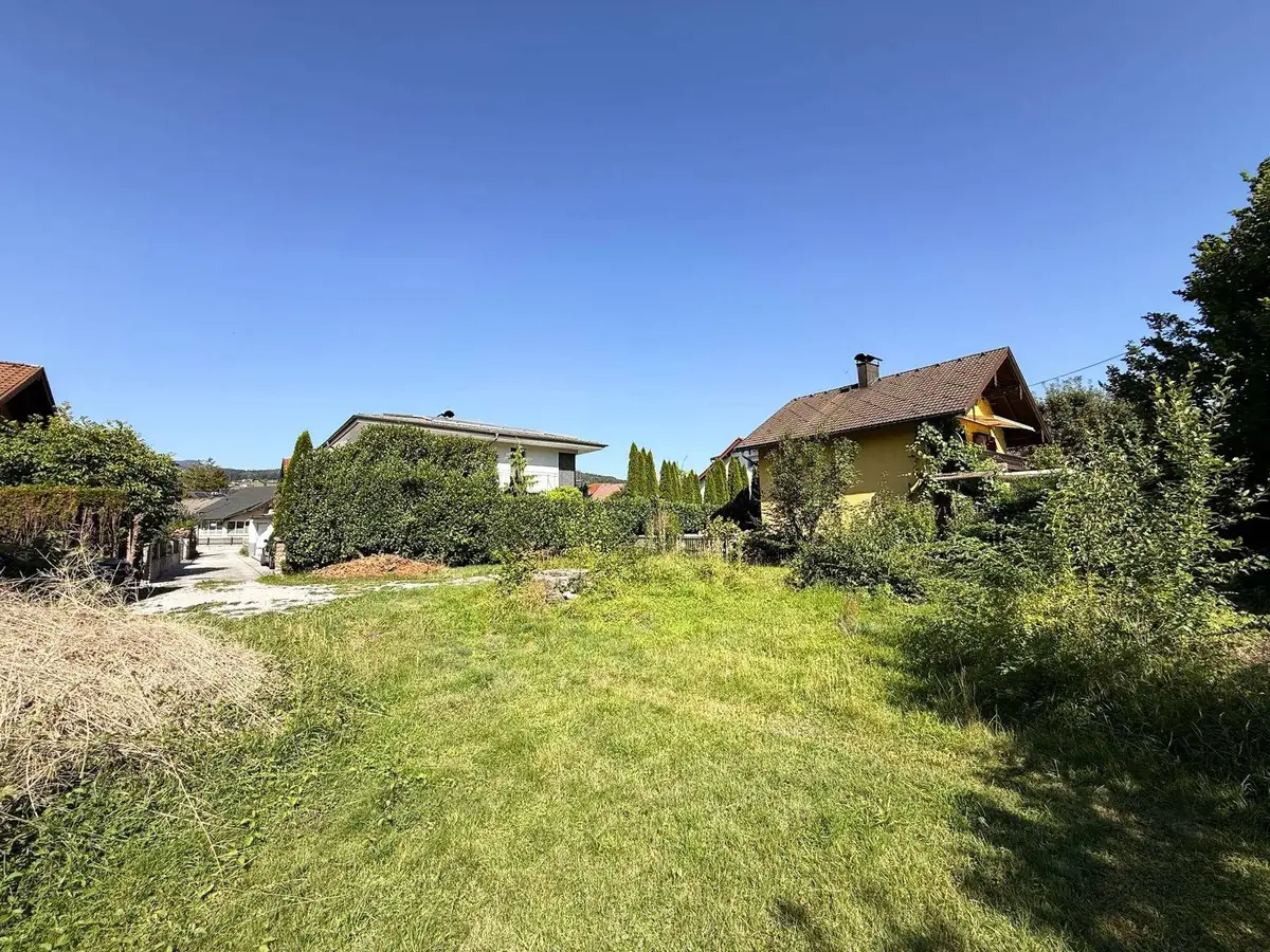 Weitläufiges grünes Grundstück unter blauem Himmel mit angrenzenden Wohnhäusern und viel Grün.