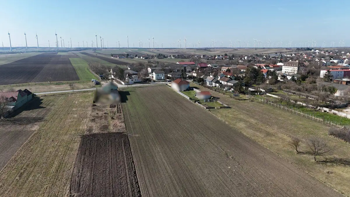 Weitläufige Luftaufnahme einer ländlichen Gegend mit Feldern, Siedlung und zahlreichen Windrädern.