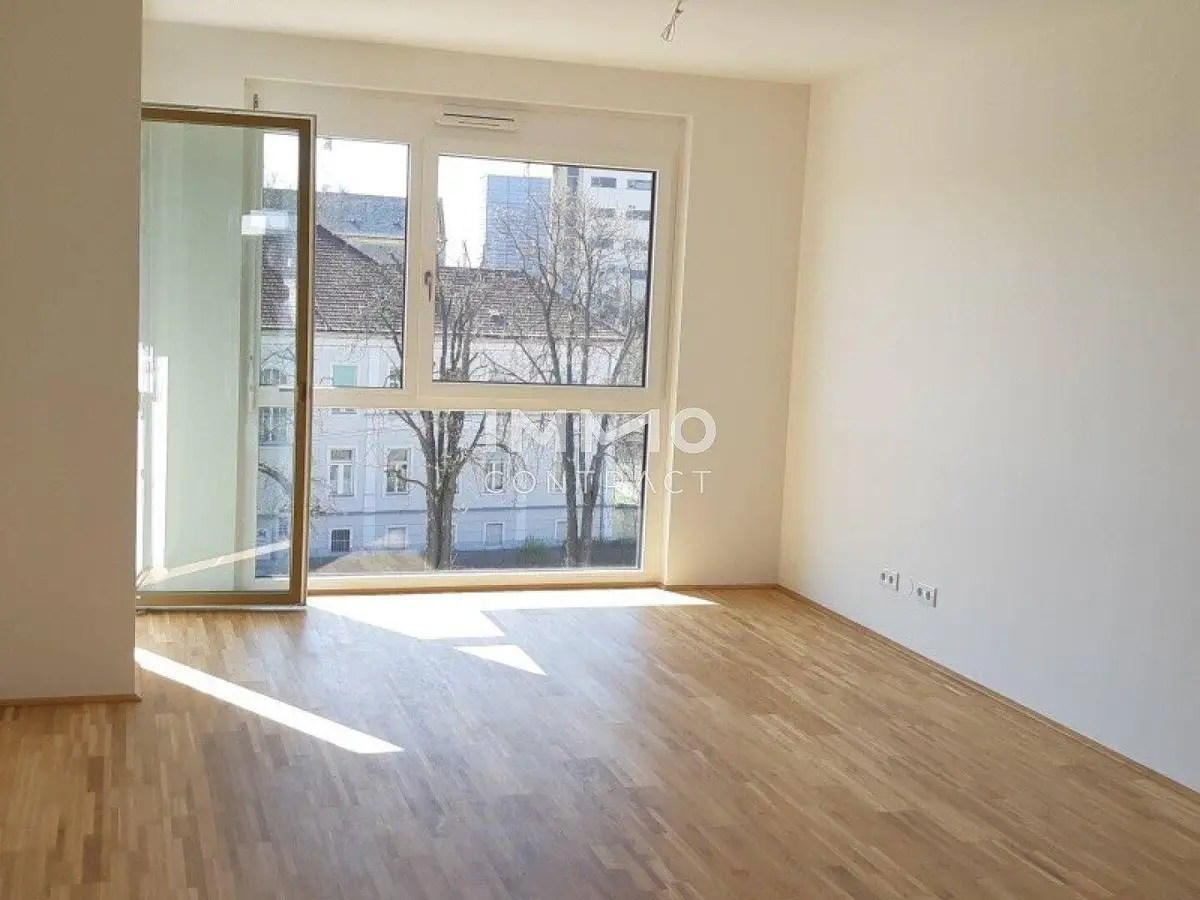 Heller Wohnraum mit großen Fenstern, Holzboden und viel natürlichem Lichteinfall.