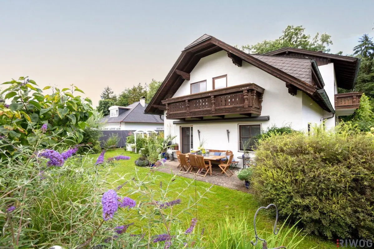 Charmantes Haus mit einer möblierten Terrasse und einem gepflegten Gartenbereich mit Blumen.