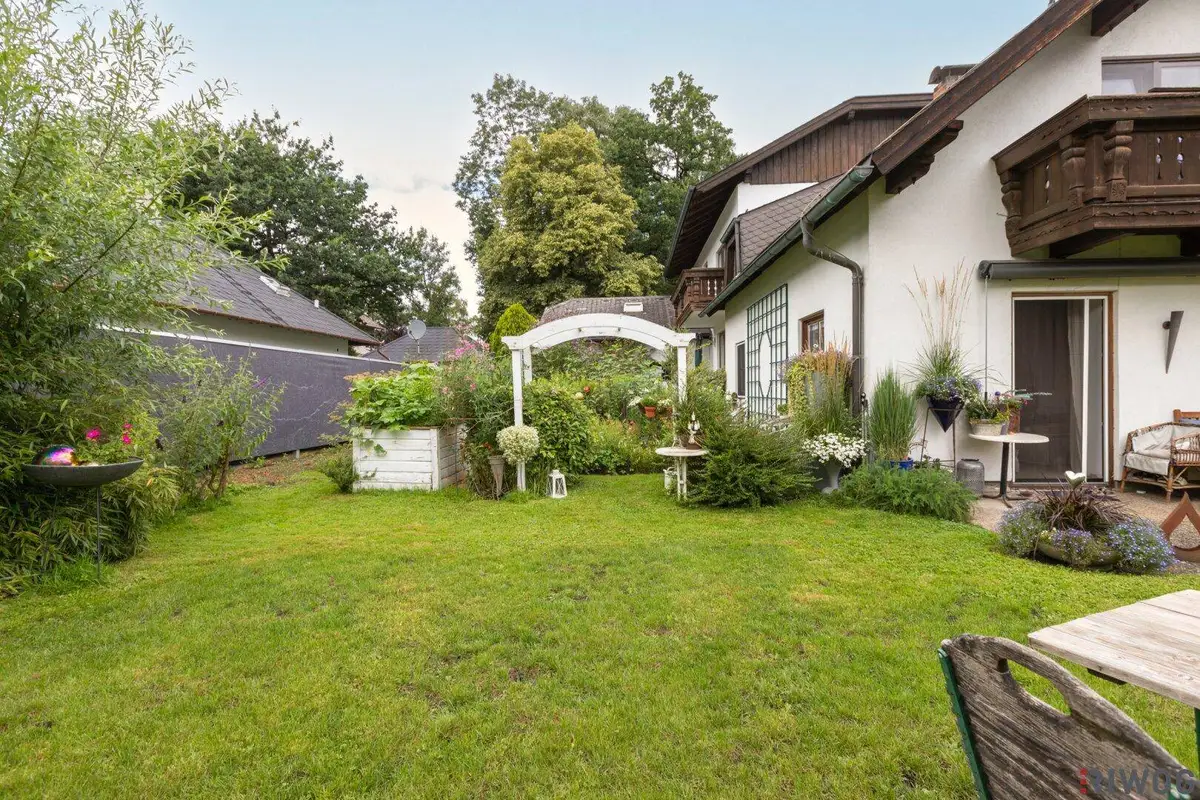 Gepflegter Gartenbereich hinter dem Haus mit Rasenfläche und dekorativem Torbogen.