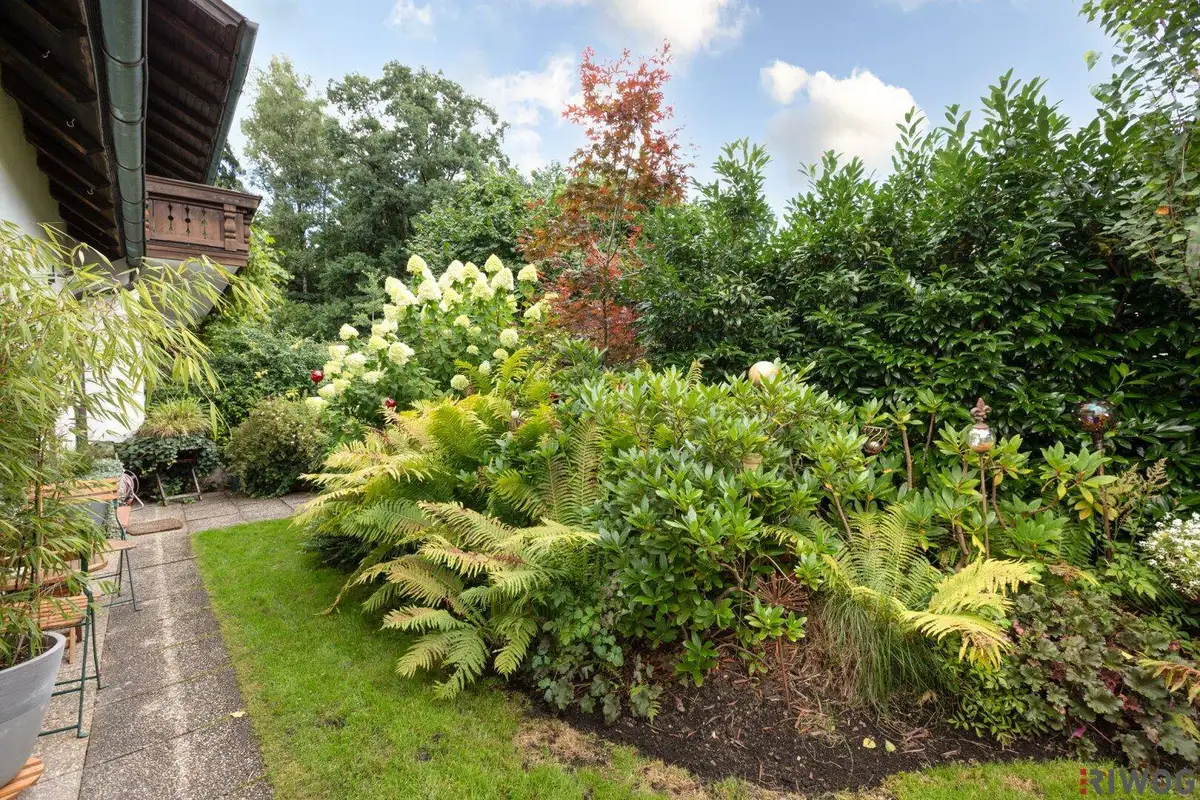 Üppiges Blumenbeet und grüne Sträucher entlang eines gepflasterten Weges im Garten.