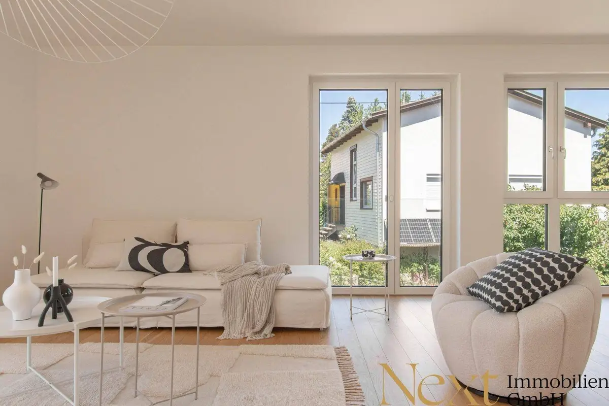Gemütlicher Wohnbereich mit beigem Sofa und Sessel, großen Fenstern und Blick auf die Nachbarschaft.