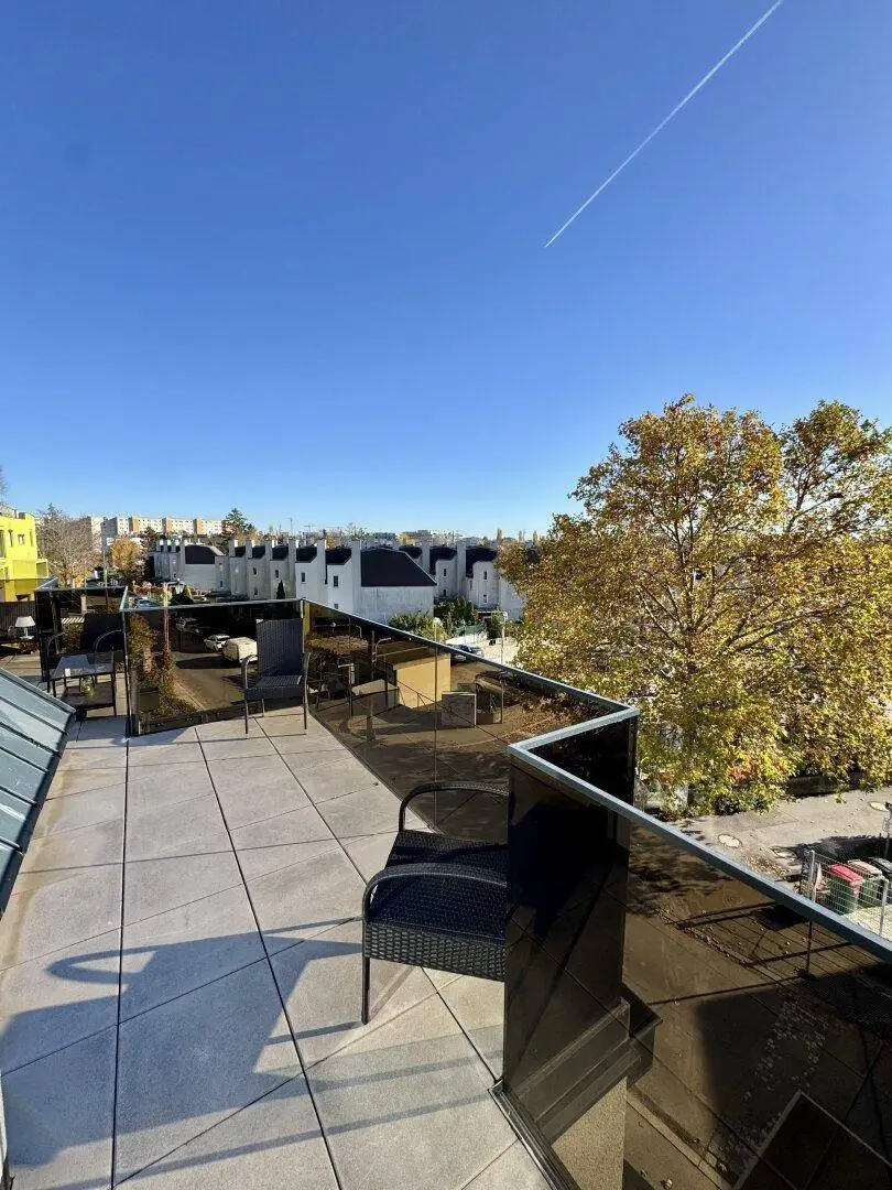 Sonniger Terrassenbereich mit dunklem Glasgeländer und einem Stuhl, um die Aussicht zu genießen.