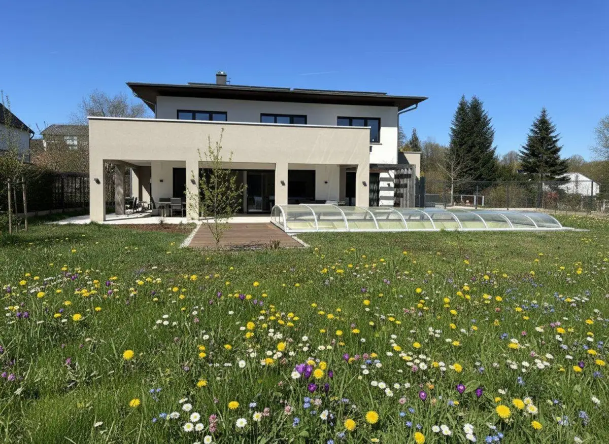 Modernes Einfamilienhaus mit großem Garten, Poolabdeckung und weitläufiger Rasenfläche mit Blumen.