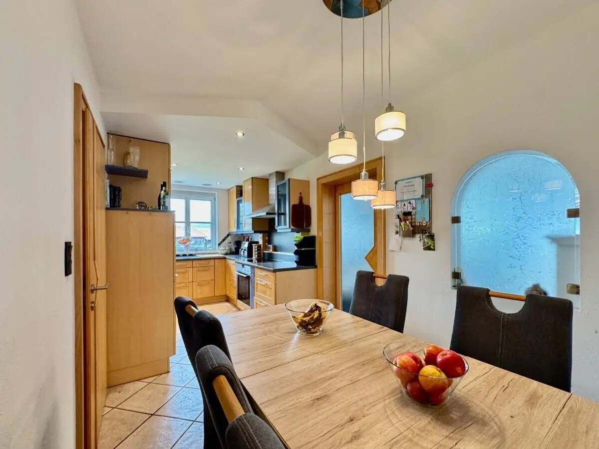 Essbereich mit Holztisch und Blick in die angrenzende Küche mit Holzfronten.