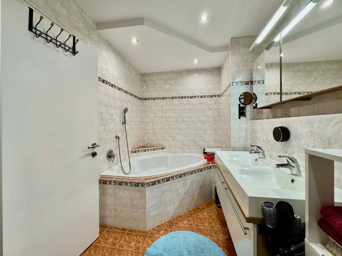 Gefliestes Badezimmer mit Eckbadewanne, Doppelwaschbecken und Spiegelschrank.