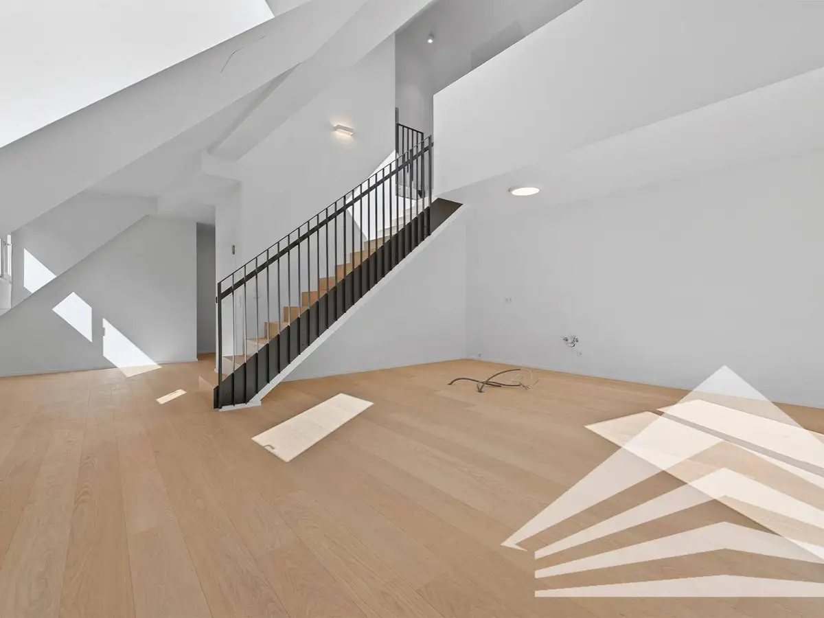 Heller, leerer Wohnbereich mit Holzfußboden, weiß gestrichenen Wänden und moderner Treppe.